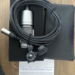 Stříbrný kondenzátorový mikrofon s mřížkou, na kterém je nápis audio-technica. Součástí je černý kabel s XLR konektory, černý držák a černý ochranný…