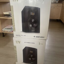 Dvě bílé krabice od studiových monitorů, jedna umístěná nad druhou. Na obou je zobrazen černý reproduktor a nápisy T7V, ADAM AUDIO a T SERIES (na hor…