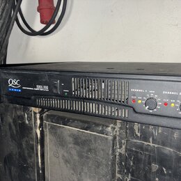 Černý výkonový zesilovač s nápisy QSC AUDIO a RMX 850 PROFESSIONAL POWER AMPLIFIER. Na předním panelu jsou dvě sekce označené CHANNEL 1 a CHANNEL 2,…