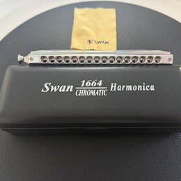 Stříbrná chromatická harmonika s kovovým povrchem a řadou otvorů. Vedle ní je černý plastový obal s bílým nápisem Swan 1664 CHROMATIC Harmonica. V po…