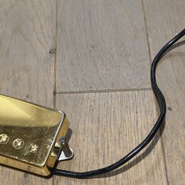 Zlatý humbucker s kovovým krytem a šesti viditelnými šrouby v polosičce. K snímači vede černý kabel s odhalenými koncovými vodiči a bílým papírovým š…