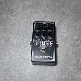 Černý kytarový efekt s nápisy METAL MUFF a electro-harmonix NEW YORK CITY, USA. Na horní straně jsou čtyři černé ovládací knoflíky a popisky TREBLE,…