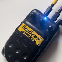 Černý efekt pedál s žlutým štítkem, na kterém je nápis THRASHMETAL a pod ním logo SOUNDTANK TMS. Nad hlavním nápisem jsou označení LEVEL, TONE a DIST…