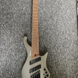 Stříbrná elektrická basa s šesti strunami a hnědým hmatníkem. Na korpusu je viditelné logo Ibanez. Nástroj má černý hardware a tři ovládací knoflíky…
