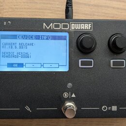 Černý kompaktní efektový procesor s nápisem MOD DWARF. Displej zobrazuje text DEVICE INFO, CURRENT RELEASE: v1.13.5.3315 a DEVICE SERIAL: MDWD02M02-0…