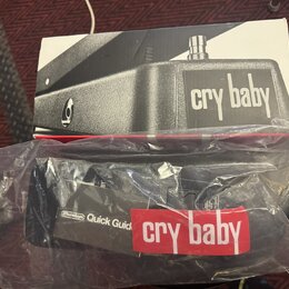 Fotografie zobrazuje krabici a plastový obal s manuálem k wah-wah pedálu. Na krabici je černobílá fotografie přístroje s nápisem cry baby. V plastové…