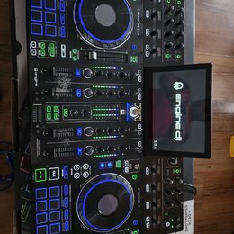 Černý DJ kontrolér Denon DJ Prime 4 s integrovaným displejem, na kterém je nápis engine dj a verze 5.0. Zařízení má dva jog-kola s modrým podsvícením…