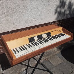 Elektronický klavír v dřevěném korpusu hnědé barvy. Na pravé straně horní desky je nápis weinmeister Clavisei a pod ním označení 2000. Nástroj má bíl…