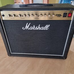 Kytarový kombo zesilovač značky Marshall, model DSL 40C. Má černý potah a bílý lem kolem mřížky reproduktoru. Na horním ovládacím panelu jsou umístěn…