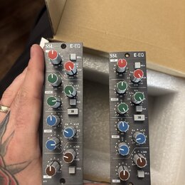 Dvě identické šedé rackové jednotky s nápisy SSL E-EQ. Každý modul obsahuje několik barevných otočných knoflíků (červený, zelený, modrý a hnědý) a př…