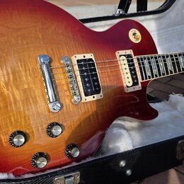 Elektrická kytara s tvarem single-cutaway a povrchovou úpravou v červeně-žlutém sunburstu s viditelnou strukturou dřeva. Nástroj má dva humbuckery v…