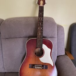 Akustická kytara s dreadnought tělesem v červeně-žlutém sunburst provedení a bílým pickguardem. Hmatník je tmavý s bílými tečkovanými značkami a hlav…