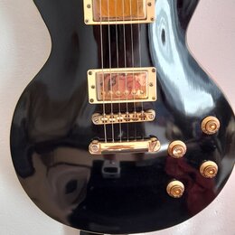 Černá elektrická kytara s gold hardwarem a hnědým hmatníkem. Na těle jsou dva humbuckery, čtyři otočné knofíky a přepínač s nápisy RHYTHM a TREBLE. P…