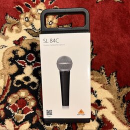 Fotografie zobrazuje bílé originální balení mikrofonu v černé plastové ochranné obálce. Na krabici je nápis SL 84C Dynamic Cardioid Microphone, logo…