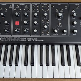 Černý semi-modulární analogový syntetizátor s bílými klávesami. Na předním panelu je nápis GRANDMOTHER SEMI-MODULAR ANALOG SYNTHESIZER a logo moog. P…