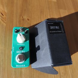 Zelený efekt pedál s nápisy OVERDRIVE, GREEN MILE a MOGER. Má dva ovládací knoflíky označené LEVEL a TONE, přepínač a stoupací spínací tlačítko. Vedl…