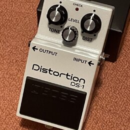 Bílý efekt pedál s nápisy Distortion a DS-1. Na horní části jsou tři ovládací knoflíky s popisky LEVEL, TONE a DIST a červená kontrolka s nápisem CHE…