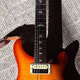 Elektrická kytara s žlutě-oranžovým přechodem (sunburst) a viditnou strukturou dřeva. Na hlavě je červený lak a bílý nápis PRS. Hmatník má vložky ve…