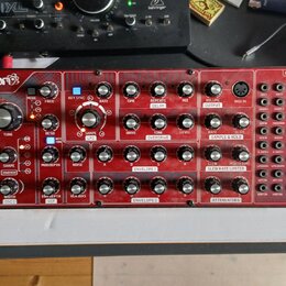 Červený semi-modulární syntetizátor s nápisy behringer a NEUTRON. Přední panel obsahuje zahlreichetočítka, přepínače a patchovací pole s označením IN…