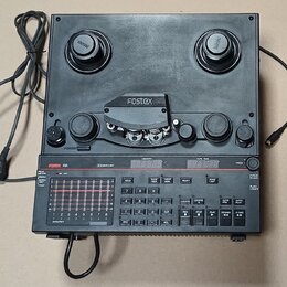 Černý elektronický přístroj s nápisem FOSTEX R8. Horní část obsahuje dvě cívky s logem Fostex a mechanismus pro pásku pod krytem s nápisem Fostex. Sp…