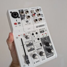 Bílá mixovací konzole Yamaha AG03. Na horní části jsou vstupy pro mikrofon, kytaru a linkové vstupy s nápisy „GUITAR“, „MONO“ a „LINE“. Přední panel…