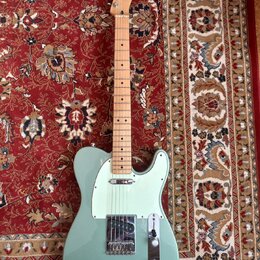 Světle zelená elektrická kytara typu Telecaster s javorovým hnedem. Na hlavě je viditelné logo Fender. Kytara má bílý pickguard a chromované kovové č…
