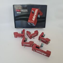 Krabice a pět červených triggerů značky ddrum. Na krabici jsou nápisy ACOUSTIC PROTRIGGERS, ddrum, SNARE TRIGGER a CONTAINS: 3x TOM, 1x SNARE, 1x KIC…
