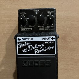 Černý kytarový efekt pedál značky BOSS. Na horní straně jsou čtyři ovládací knoflíky s nápisy LEVEL, CHECK, VIBRATO a COSM. Na přední straně je bílá…