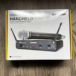 Fotografie znázorňuje krabici s bezdrátovým mikrofonním systémem. Na obalu je nápis CONCERT HANDHELD Frequency-Agile UHF Wireless System a logo SAMSO…