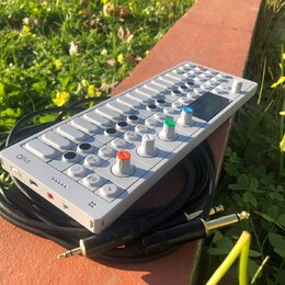 Bílý syntezátor OP-1 s klávesovou hrou a ovládacími knoflíky v různých barvách (modrý, zelený, oranžový). Na levé straně je viditelný nápis OP-1. Zař…