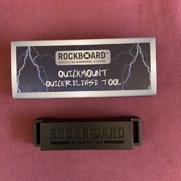 Fotografie zobrazuje černý plastový nástroj a jeho obal. Na obalu je bílý štítek s nápisy ROCKBOARD®, by WARWICK a ručně psaným textem QUICKMOUNT QUI…