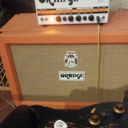 Bílý kytarový zesilovač s nápisy ORANGE a DUAL TERROR stojí na oranžovém kytarovém boxu. Box má na přední síťce logo ORANGE a nad ním dekorativní nál…