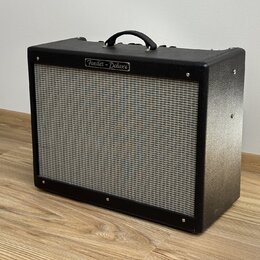 Černý kytarový kombozesilovač s texturovaným povrchem a šedou přední síťovkou. V horní části je umístěn nápis "Fender - Deluxe". Nástroj vykazuje min…