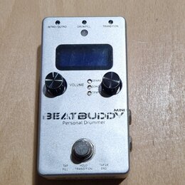 Stříbrný efekt pedál s nápisem BEATBUDDY MINI Personal Drummer. Na horní straně jsou tři tlačítka s popisky INTRO/OUTRO, DRUM FILL a TRANSITION, malý…