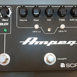 Černý kytarový pedál s bílými nápisy a logem Ampeg. V horní části jsou ovládací knoflíky s popisky Drive, Blend, Volume, Bass, Mid, Treble a AUX Leve…
