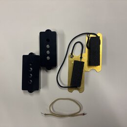 Fotografie zobrazuje dvě černé plastové krytky s otvory, zlatý kovový základ s dvěma černými pěnovými vložkami a bílý kabel. Na komponentech nejsou ž…