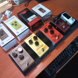 Na černém pedalboardu je umístěno pět efektových pedálů. Zleva doprava jsou vidět pedály s nápisy tc electronic Echobrain ANALOG DELAY (stříbrný), tc…