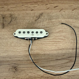 Bílý snímač typu single-coil s šesti černými póly, umístěný v černém plastovém rámečku. Na bílém krycí desce je vidět nečitelný nápis a symbol. Ze sp…
