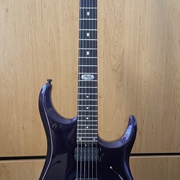 Tmavě fialová elektrická kytara s černým hmatníkem a dvěma humbuckery. Na hlavě je bílý nápis MUSIC MAN. Nástroj stojí na černém stojanu před dřevěno…