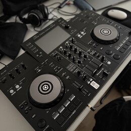 Černý DJ 컨트롤러 s dvěma jogovými koly a centrálním mixážním sekcí. Na levé straně je viditelný nápis XDJ-RR a v pravé části logo Pioneer DJ. Za přístro…