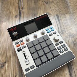 Světle šedý sampler s názvem MPC SAMPLE. Zařízení obsahuje 16 gumových padů, několik ovládacích knoflíků a řadu tlačítek s různými popisky, včetně lo…