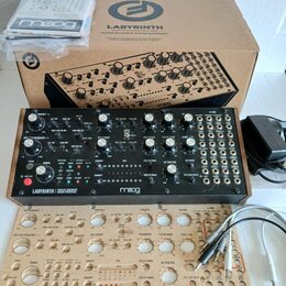 Fotografie zobrazuje analogový syntetizátor Moog Labyrinth v černé barvě s bílými nápisy a ovládacími prvky. Nástroj je doprovázen originálním kartón…