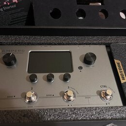 Stříbrný efektový procesor s nápisem AMPERO a podtitulem Amp Modeler & Effects Processor. Zařízení má centrální displej, dva otočné ovladače s popisk…