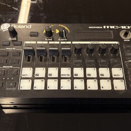 Černá groovebox s bílými popisky a tlačítky. Na horní hraně je nápis Roland vlevo a GROOVEBOX MC-101 vpravo. Zařízení obsahuje několik ovládacích kno…