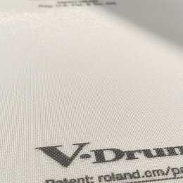 Bílá bubnová plocha s jemnou mřížkovou strukturou. V horní části je logo Roland a pod ním nečitelný text. Ve spodní části je velký nápis V-Drums a po…