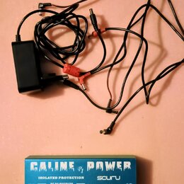 Černý napájecí adaptér s připojenými kabely a několika konektory. Vedle něj je modrá krabička s bílým nápisem CALINE P1 POWER, ISOLATED PROTECTION a…