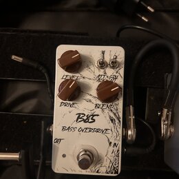 Bílý kytarový efekt s nápisy B85 a BASS OVERDRIVE. Na horní straně jsou tři hnědé otočné knoflíky s popisky LEVEL, DRIVE a BLEND a dva přepínací spín…