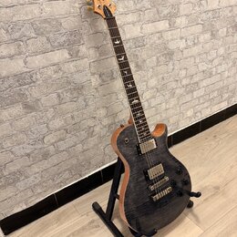 Elektrická kytara s tmavým, pruhovaným povrchem těla a světle hnědými hranami. Na hlavě je viditelné logo značky Cort. Nástroj má dva humbuckery, tři…