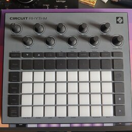 Šedý sampler Novation Circuit Rhythm s bílými podsvícenými pady v mřížce 4x8. V horní části jsou umístěny otočné ovladače s popisky Master Volume, Tu…