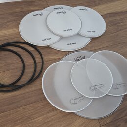 Sada bílých bubnových blan v různých velikostech a tři černé gumové prstence. Pět blan nese nápisy drum-tec a real feel, další čtyři mají nápis Mille…